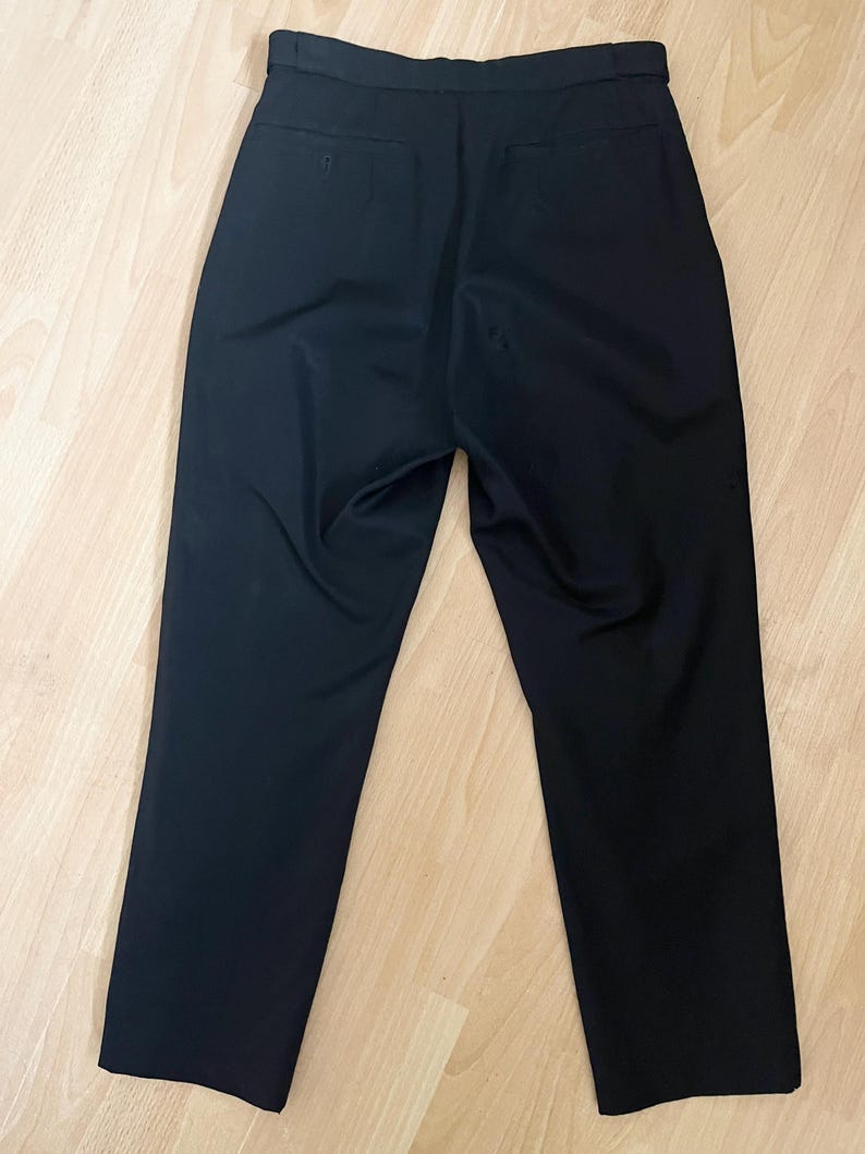 May include: Black dress pants with a high waist and a straight leg. The pants have two back pockets and a button and zipper closure. The fabric appears to be a smooth, woven material.