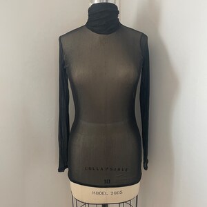 May include: Black sheer long-sleeved turtleneck top with a fitted silhouette. The top is made of a lightweight, breathable fabric and has a slightly loose fit. The top is labelled "COLLAPSIBLE 10 KODEL 2005".