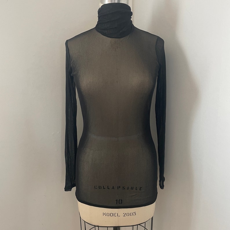 May include: Black sheer long-sleeved turtleneck top with a fitted silhouette. The top is made of a lightweight, breathable fabric and has a slightly loose fit. The top is labelled "COLLAPSIBLE 10 KODEL 2005".