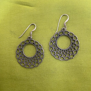 May include: A pair of silver earrings with a delicate, circular, openwork design. The earrings have a simple hook closure.