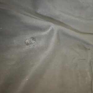 May include: A close-up shot of a dark, possibly black, fabric with a slightly textured surface. There is a small, irregular patch of lighter color and texture near the center. The fabric appears to be folded or draped.