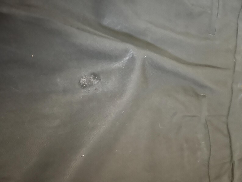 May include: A close-up shot of a dark, possibly black, fabric with a slightly textured surface. There is a small, irregular patch of lighter color and texture near the center. The fabric appears to be folded or draped.