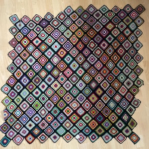 May include: A black crochet blanket with a colorful geometric pattern. The blanket is made up of many small squares, each with a different color and design.