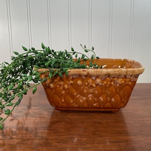 May include: A rectangular ceramic planter with a glossy amber-brown finish and a textured diamond-patterned exterior. The rim features a decorative drip-glaze effect in a lighter cream color. A trailing green string of pearls plant hangs over.
