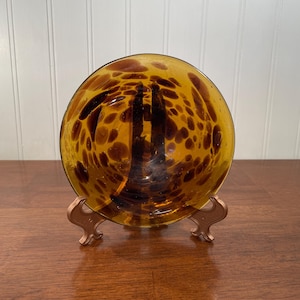 May include: A brown glass bowl with a leopard print design on a gold metal stand.