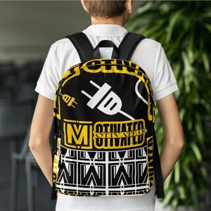 K&ouml;nnte beinhalten: Schwarzer Rucksack mit gelbem und wei&szlig;em Design. Der Rucksack hat eine gro&szlig;e wei&szlig;e Steckergrafik und die W&ouml;rter "Motivated" und "Otivated" in gelben Buchstaben.