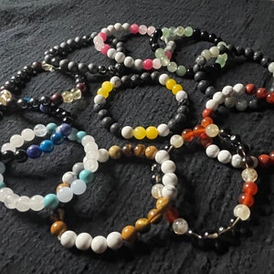 May include: A collection of 10 beaded bracelets in various colours and materials, including black lava rock, white howlite, red carnelian, yellow jasper, green aventurine, blue lapis lazuli, and tiger's eye.