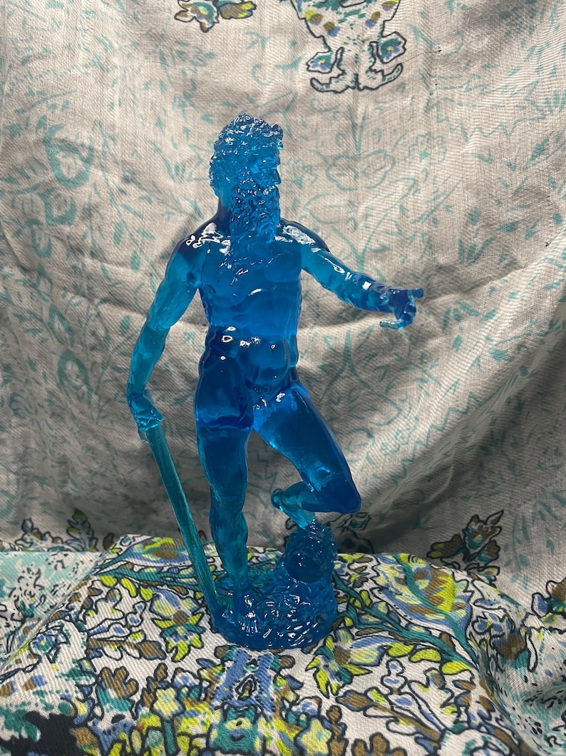 K&ouml;nnte beinhalten: Eine durchscheinende blaue Figur eines b&auml;rtigen Mannes, m&ouml;glicherweise Neptun oder Poseidon, der einen Dreizack h&auml;lt. Die Figur steht auf einem Sockel, mit detailliertem Bart und Haaren. Die Figur besteht aus einem klaren, m&ouml;glicherweise Harzmaterial.
