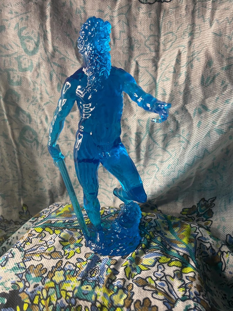 K&ouml;nnte beinhalten: Eine durchscheinende blaue Figur eines b&auml;rtigen Mannes, m&ouml;glicherweise eine mythologische Figur, die einen Stab h&auml;lt. Die Figur steht auf einer wellenartigen Basis. Die Figur ist etwa 15 cm gro&szlig;.