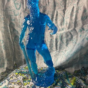 K&ouml;nnte beinhalten: Eine durchscheinende blaue Figur eines Mannes mit langem Bart, der einen Stab h&auml;lt. Die Figur steht auf einem strukturierten Sockel. Die Figur besteht aus einem klaren, gl&auml;nzenden Material.