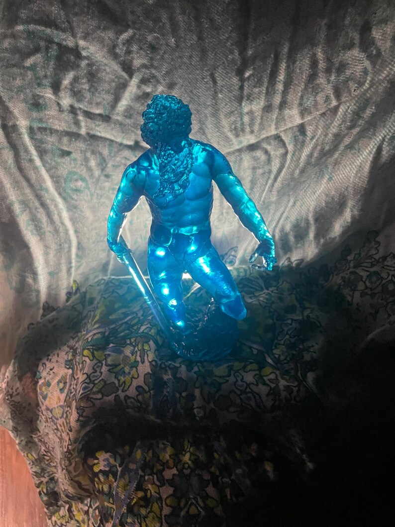 K&ouml;nnte beinhalten: Eine durchscheinende blaue Figur eines muskul&ouml;sen Mannes mit Bart, der einen Stab h&auml;lt. Die Figur ist in einer dynamischen Haltung dargestellt, wobei das Licht durch sie hindurchscheint. Die Figur ist ein dekorativer Gegenstand.