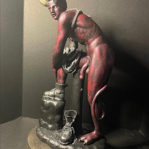 May include: A red-skinned, horned humanoid figurine with yellow eyes, leaning against a central pillar. The figure has a tail, wears a harness, and stands on a base with two black boots, one worn on a foot and one placed on the ground nearby.