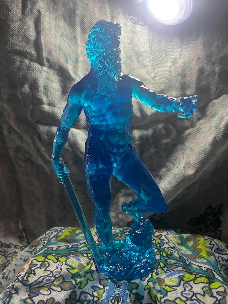 K&ouml;nnte beinhalten: Eine durchscheinende blaue Skulptur eines Mannes mit Bart, der einen Stab h&auml;lt. Die Figur ist mit einem Bein nach vorne und einem ausgestreckten Arm posiert und scheint zu zeigen. Die Skulptur steht auf einem Sockel, der Wasser &auml;hnelt.