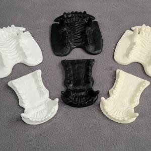 Puede incluir: Seis piezas decorativas detalladas y estilizadas. Dos son negras y cuatro son blancas. Las piezas tienen un diseño texturizado con una apariencia esquelética u orgánica. Los objetos están dispuestos sobre una superficie gris.