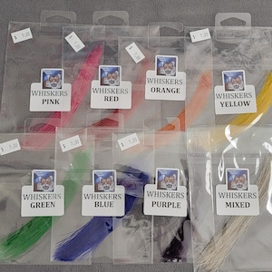 Puede incluir: Una colección de bigotes coloridos en bolsas de plástico transparente. Cada bolsa está etiquetada con un nombre de color: Rosa, Rojo, Naranja, Amarillo, Verde, Azul, Morado y Mezclado. Las etiquetas presentan un tigre de dibujos animados.