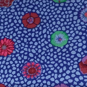 Op de afbeelding: Een blauwe stof met een wit stippenpatroon en kleurrijke bloemenontwerpen. De bloemen zijn rood, roze, groen en blauw.