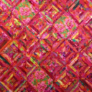May include: A quilt made of colorful fabric scraps in shades of red, pink, and orange. The fabric is patterned with flowers and geometric designs. The quilt is stitched together in a diamond pattern.