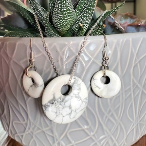 May include: A white howlite stone necklace and earrings set with silver chain and hooks. The stones are round with a hole in the center and have a marbled pattern.