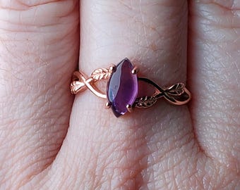 May include: A rose gold ring with a purple gemstone set in a leaf design.
