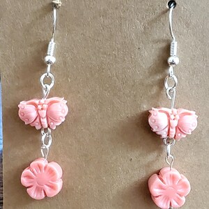 May include: A pair of pink butterfly and flower dangle earrings. The earrings are made of plastic and have a silver tone finish.
