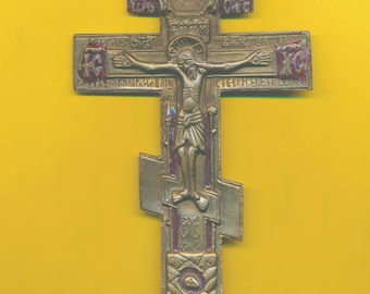 Puede incluir: Una cruz de color dorado con una representación de Jesucristo en la cruz. La cruz está decorada con esmalte rojo y morado y tiene texto cirílico.