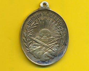 Könnte beinhalten: Eine ovale Silbermedaille mit der Aufschrift "Premio Almerito" am Rand. Die Mitte der Medaille zeigt eine Sonne mit einem Gesicht, zwei gekreuzte Federn und einen Kranz aus Blättern.