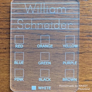 May include: Clear acrylic name and color chart with the name "William Schneider" at the top. Below are boxes labeled with colors: red, orange, yellow, blue, green, purple, pink, black, brown, and white.