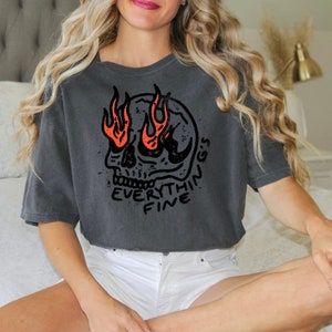 Może przedstawiać: Szary, krótki t-shirt z nadrukiem czarno-białej czaszki. Czaszka ma płomienie zamiast oczu, a pod nią znajduje się napis "EVERYTHING'S FINE".