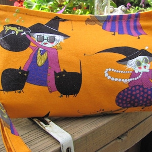 Halloween clutch or wristlet with a silly witch and her black kitties.Lining is bat pattern with orange glitter. Zip close.Handle detaches