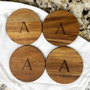 May include: Set of four round wooden coasters with the letter "A" engraved on each coaster.