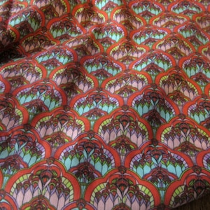 May include: Red fabric with a repeating pattern of blue, green, and pink stylized floral shapes.