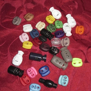 Puede incluir: Surtido de botones y cierres de cordón de plástico de colores en varias formas y tamaños. Los botones se utilizan para ajustar la longitud de los cordones, las correas y otros artículos.