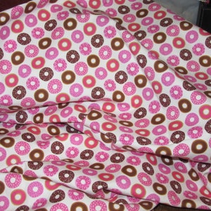 May include: White fabric with a repeating pattern of pink and brown donuts. The donuts have a white glaze and sprinkles.