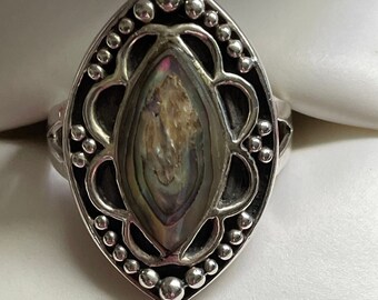 May include: A silver ring featuring a marquise-shaped abalone shell inlay at the centre. The setting is decorated with a scalloped metal border and small silver beads. The metal has a dark oxidised finish in the recessed areas to highlight the details.