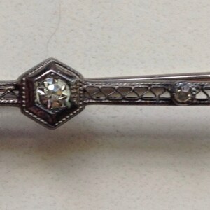 May include: A silver filigree brooch with a large clear rhinestone in the center and smaller rhinestones on the sides.