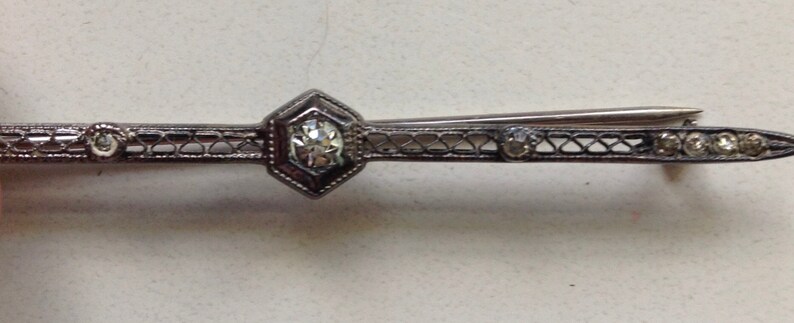 May include: A silver filigree brooch with a large clear rhinestone in the center and smaller rhinestones on the sides.