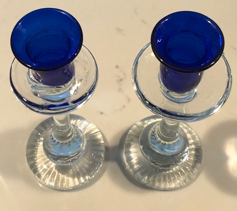 May include: Two clear glass candle holders with blue glass candle cups. The candle holders have a fluted base and a clear glass stem.