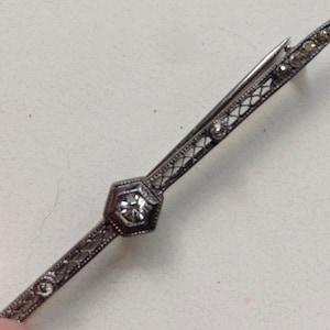 May include: A silver brooch with a delicate filigree design and a single clear rhinestone in the center.