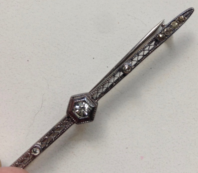 May include: A silver brooch with a delicate filigree design and a single clear rhinestone in the center.