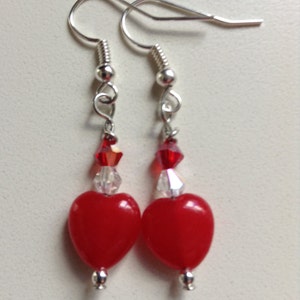 May include: A pair of silver dangle earrings with red heart-shaped beads and clear crystal accents.