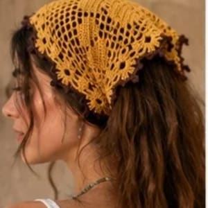 May include: A triangular crochet headscarf featuring a mustard yellow openwork pattern with a dark brown scalloped edge. The accessory is crafted with a detailed lattice design and a decorative border that frames the edges of the fabric.