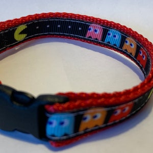 May include: Red and black pet collar with a Pac-Man design. The collar has a black plastic buckle.