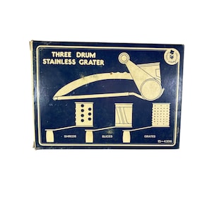 Puede incluir: Caja vintage con fondo azul e ilustraciones blancas de un rallador de acero inoxidable de tres tambores. La caja muestra el diseño del rallador y las diferentes opciones de corte: desmenuzar, rebanar y rallar.