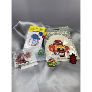 May include: An assortment of iron-on patches featuring a smiling face, a clown, a tiger, a four-leaf clover, and two ladybugs. The patches are packaged in clear plastic bags with labels that say "Sew Perfect Appliques" and "Mono-Quick".