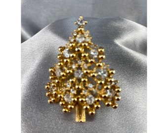 May include: A gold-tone Christmas tree brooch with clear rhinestones. The brooch is a festive and sparkly accessory for the holiday season.
