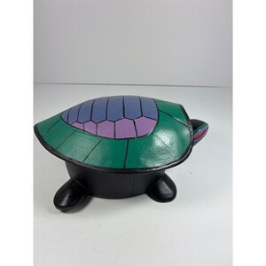 May include: A decorative turtle figurine with a green shell featuring blue and purple geometric patterns. The turtle's body is black, and its head has red and purple accents. The figurine is a unique home decor item.