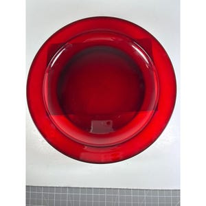 Puede incluir: Un cuenco de cristal de color rojo intenso, de forma circular, visto directamente desde arriba. El cuenco presenta una superficie lisa y translúcida con un borde ancho y plano que se transforma en una cuenca central circular hundida.