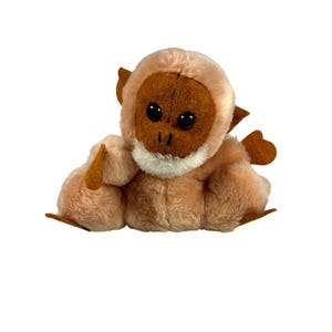 May include: A plush monkey toy with a light brown body, a darker brown face, and large black eyes. The monkey has small brown ears and hands, and a white patch of fur around its mouth. The toy is sitting upright.