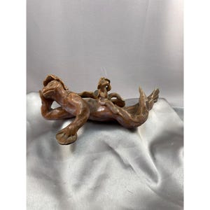 May include: A ceramic sculpture of a brown frog with a smaller frog on its back. The larger frog is lying on its side with its head resting on its arm. The smaller frog is sitting on the larger frog's back, looking up.