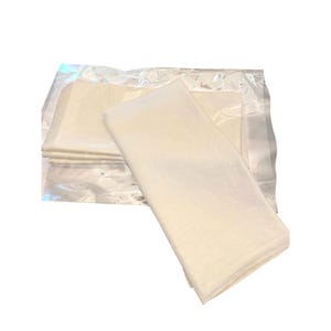 May include: A stack of off-white, rectangular sheets, possibly fabric or paper, are partially visible inside a clear plastic package. One stack of sheets is outside the package, with a slightly textured surface. The background is white.